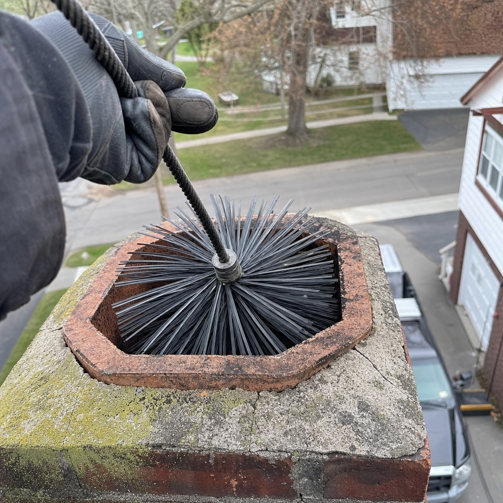 Professional chimney sweep performing maintenance with a brush on a brick chimney